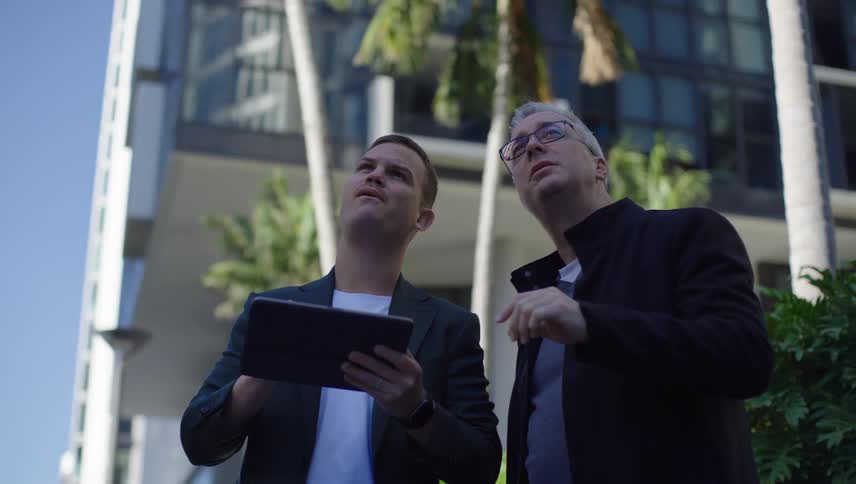 Two men talking in an outdoor area with one of them taking notes on a tablet