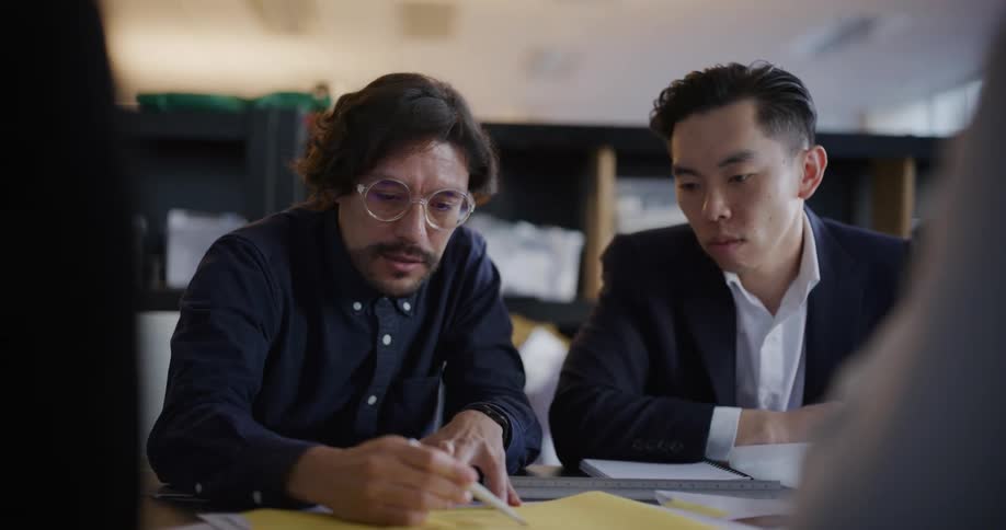 A worker talks to his coworkers about his work which he shows them by drawing something on a piece of paper in an office