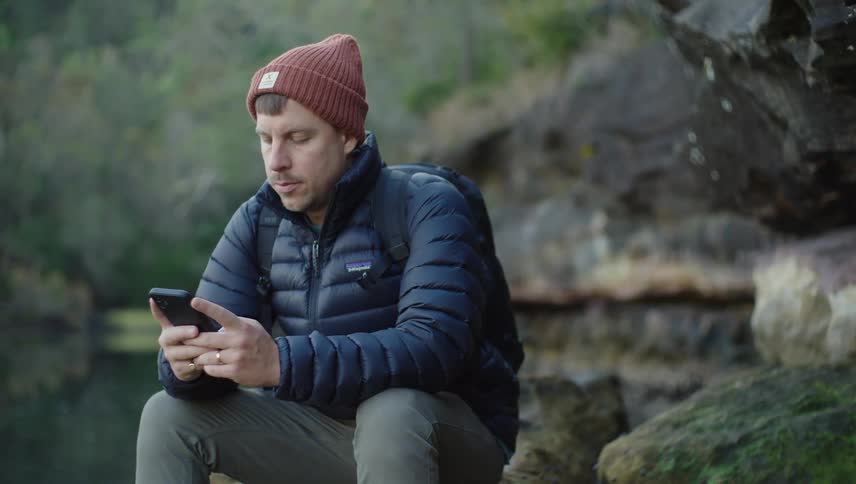 A backpacker sitting on a rock looking at his smart phone