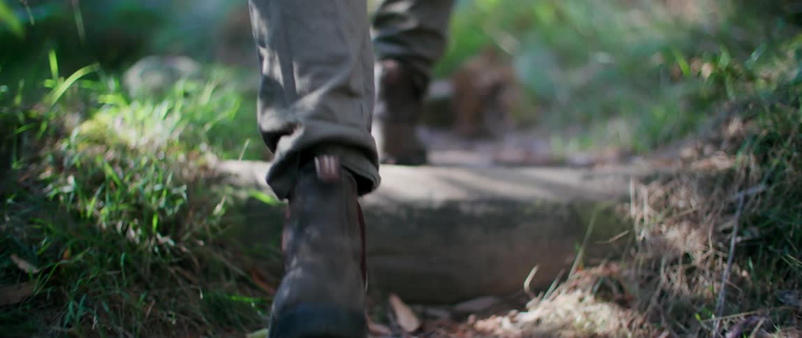 Person wearing hiking boots walks up steps on a narrow trail