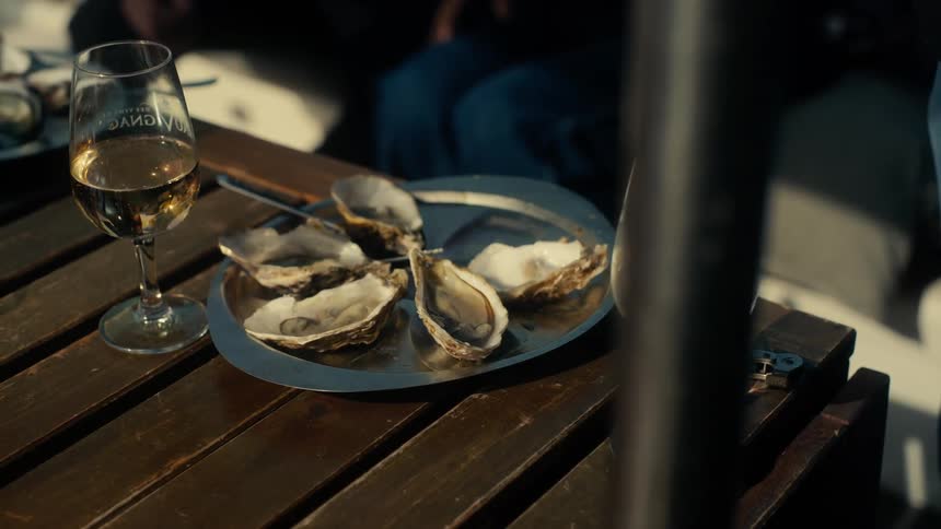 Plate with oysters and glasses with wine on a wooden table
