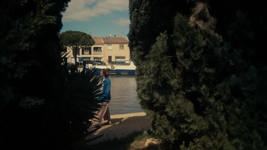 Woman strolls along the waterfront across the water from a boat at dock near an apartment building