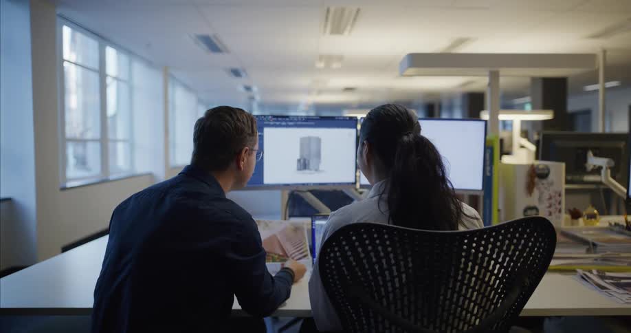 Two people sitting at a desk in an office environment working on computers