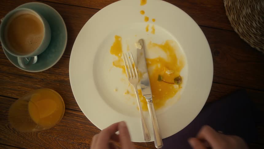 A pair of hands places a knife and fork together on a used plate with traces of gravy