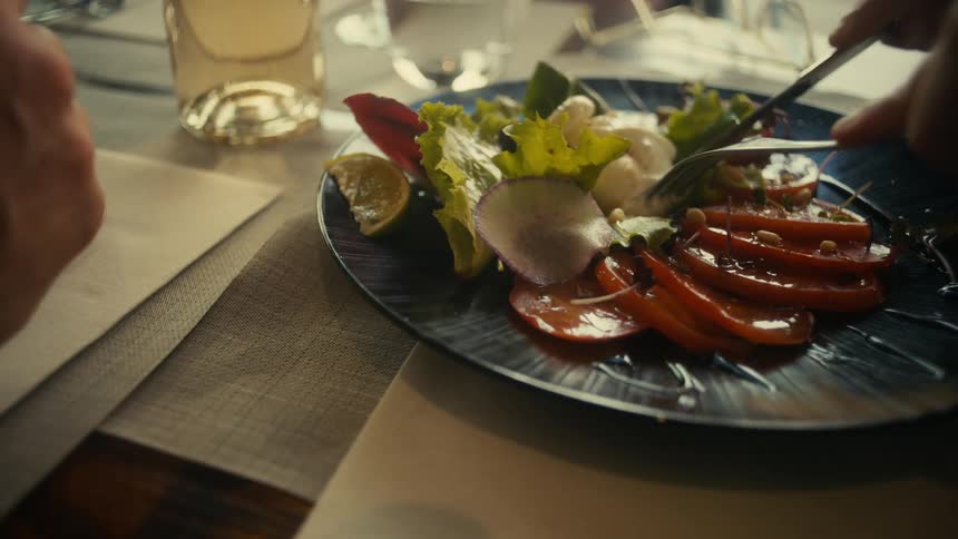 Hand holding knife and fork and cutting a salad on plate