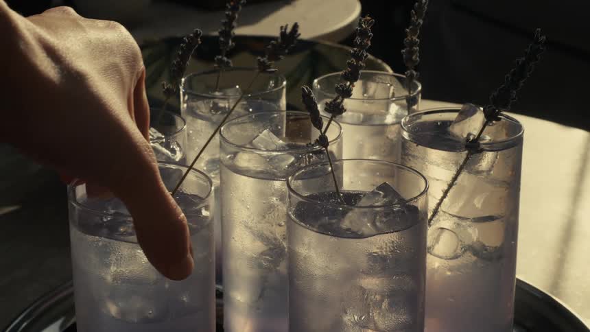 Woman puts down and picks up a glass onto and from a serving tray with other glasses