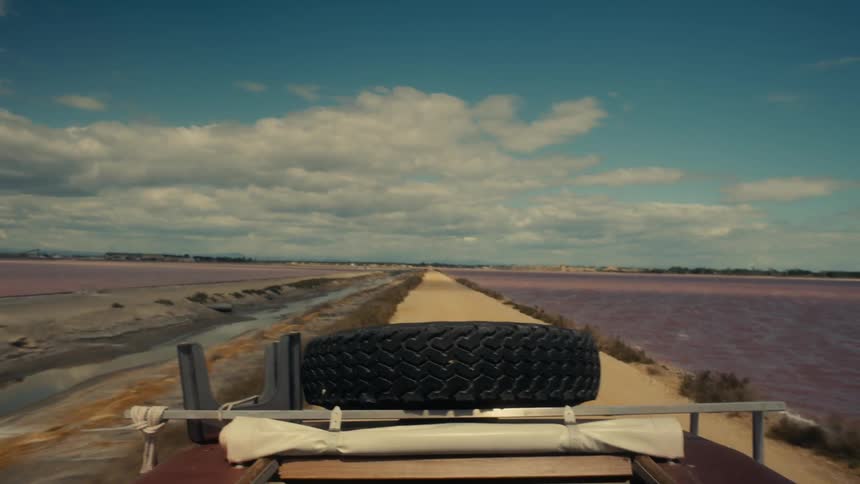 A vehicle drives on the dirt road by the shore