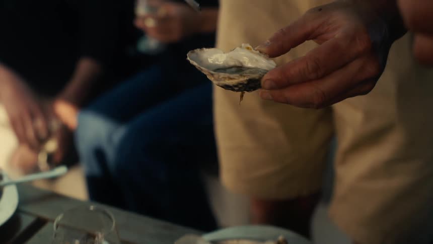 Hand picking up an oyster from a plate with several open oysters