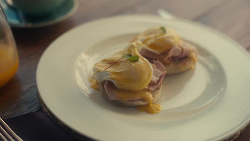 A person sets a plate of eggs benedict on top of a wooden table