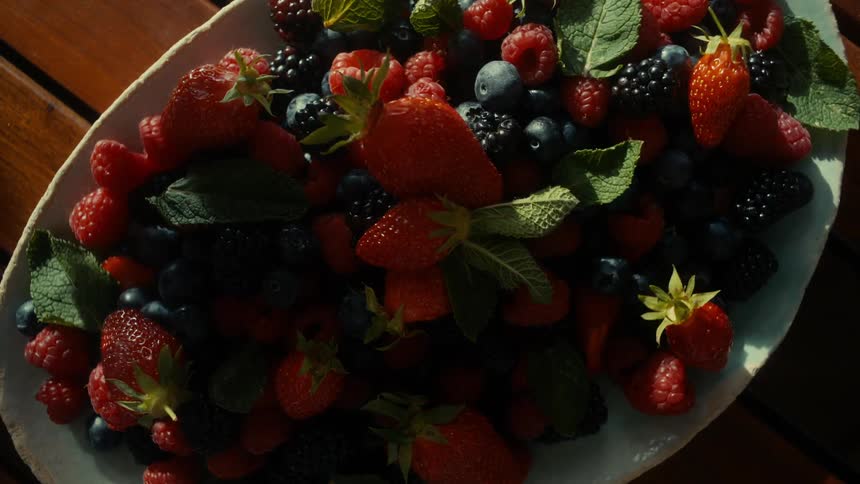 Shadows of people move over a plate of various berries sitting on a wooden picnic table