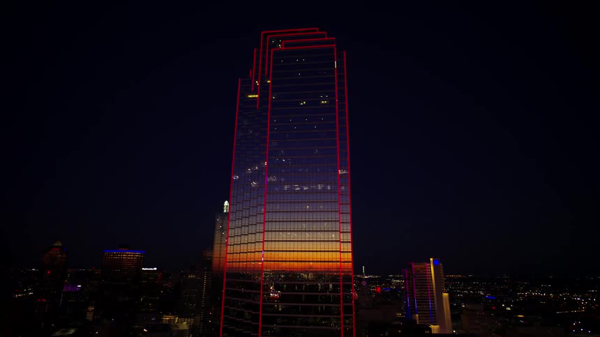 Tall skyscraper outlined in red lights reflects the red horizon at night