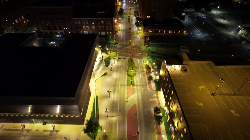 Night aerial view of an illuminated urban area with streets buildings and a visible parking lot