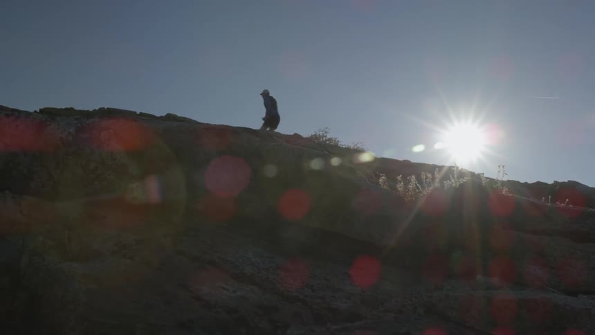 A man is jogging up a hill under a bright sun