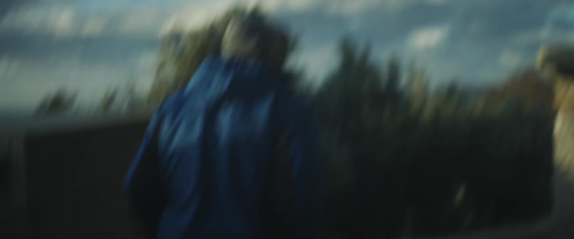 Man wearing hood walks past homes on a cloudy day