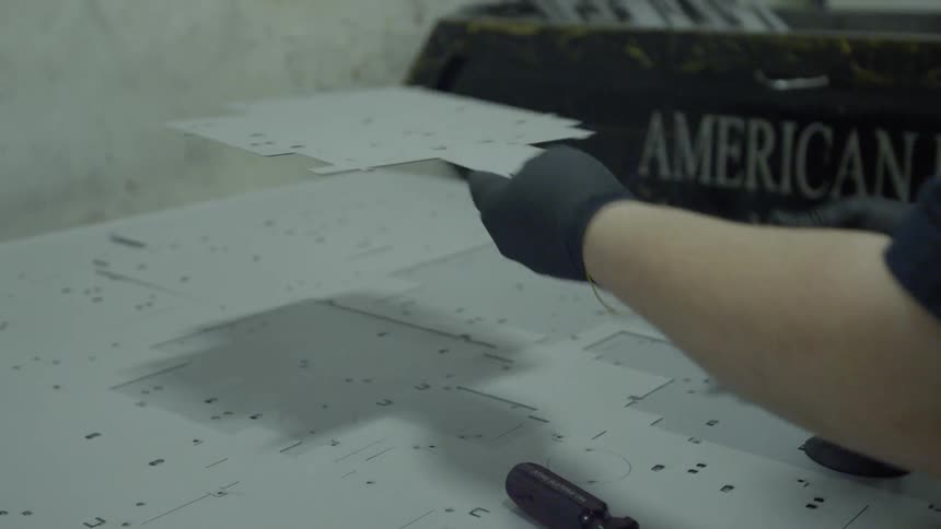 A person is lifting a piece of fabricated metal from a sheet