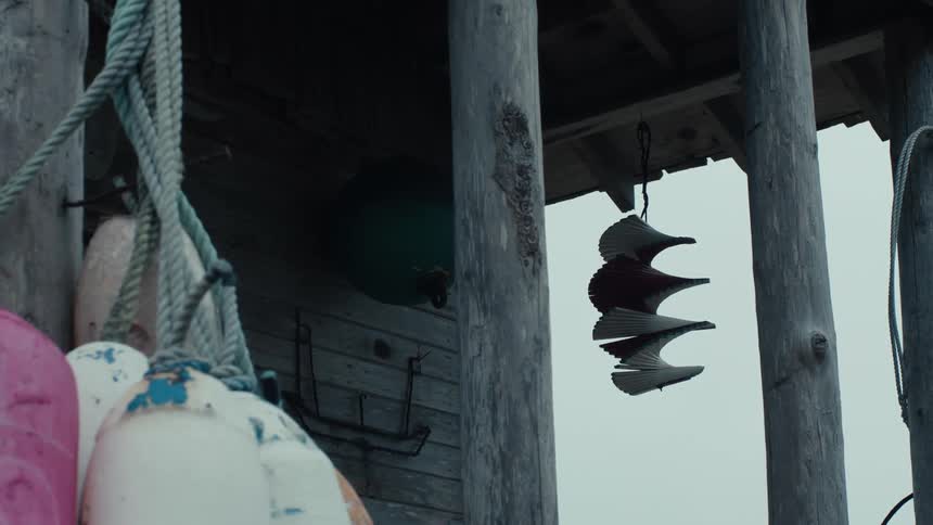 A weathered wooden structure adorned with colorful buoys and a spiral wind chime stands against a cloudy sky evoking a sense of coastal tranquility