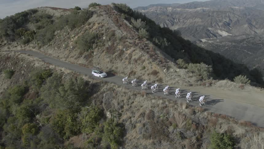 A suv following behind cyclists riding along a mountain cliff