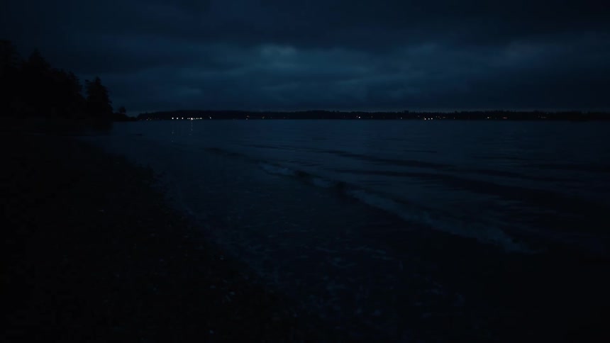 A dark moonless night with a calm body of water reflecting the distant lights of a city