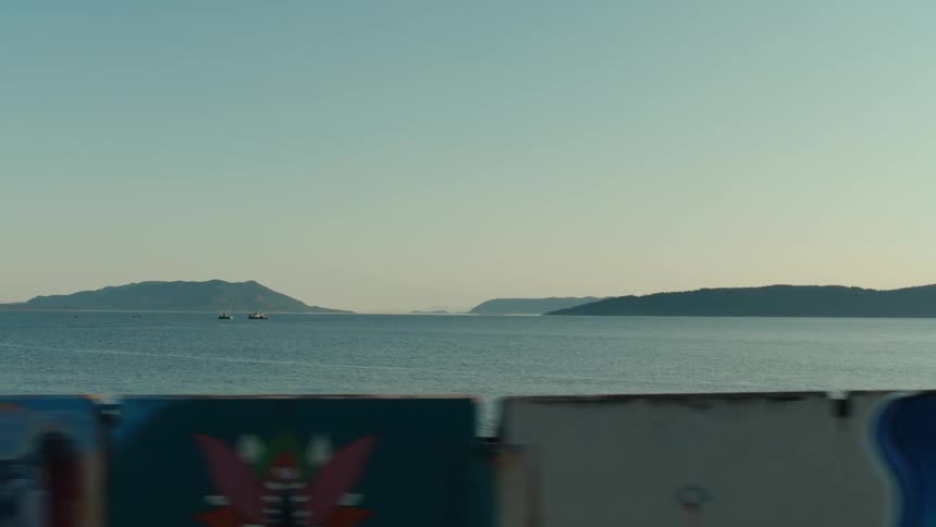 Wo small boats sail across a calm sea towards a distant island as seen from the window of a moving car