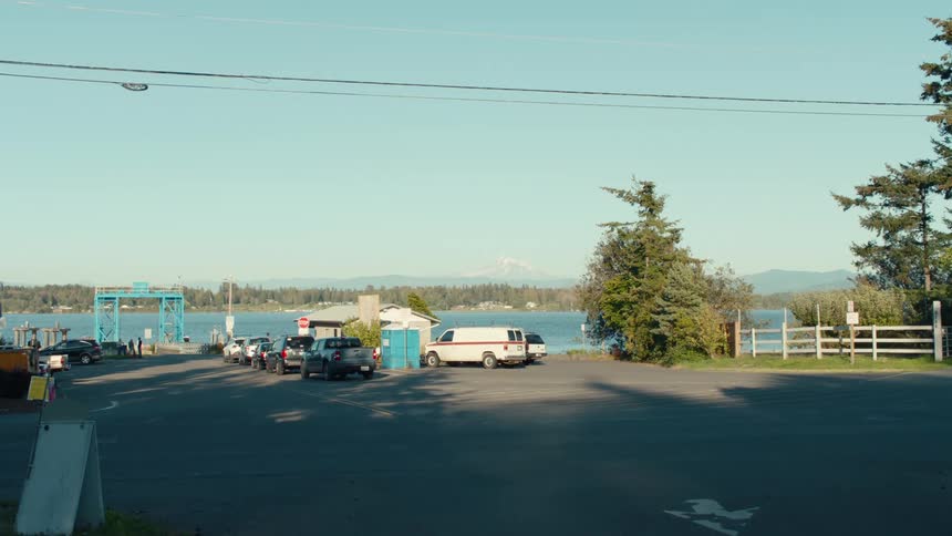 Two people riding bicycles and in the background a line of cars waiting for a ferry boat