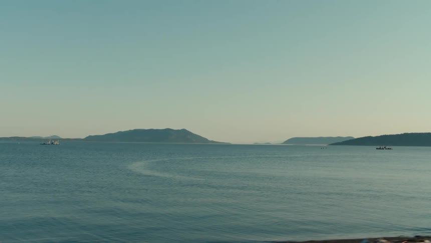 A calm body of water with small boats and low distant mountains on the horizon