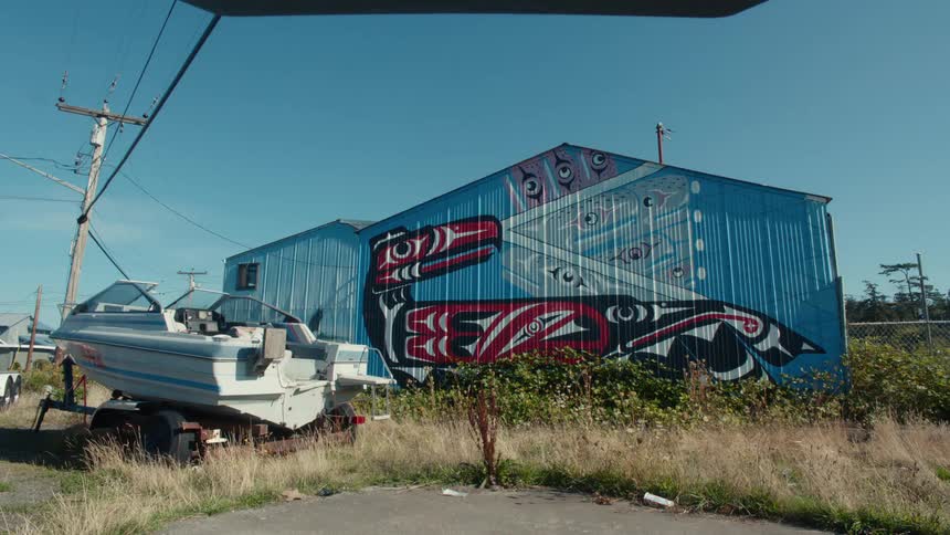 A colorful mural depicting a stylized bird adorns the side of a blue building and a white boat trailer sits in the foreground