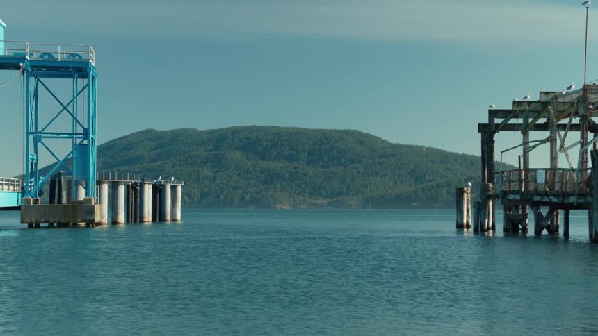 Landscape of a pier and harbor with the blue sea and forested mountains in the background