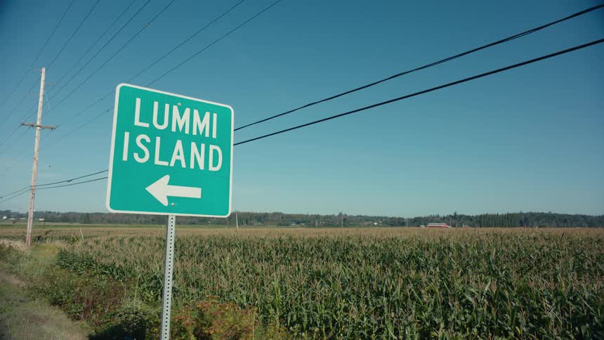 Sign providing directions stands near a crop field on a sunny day