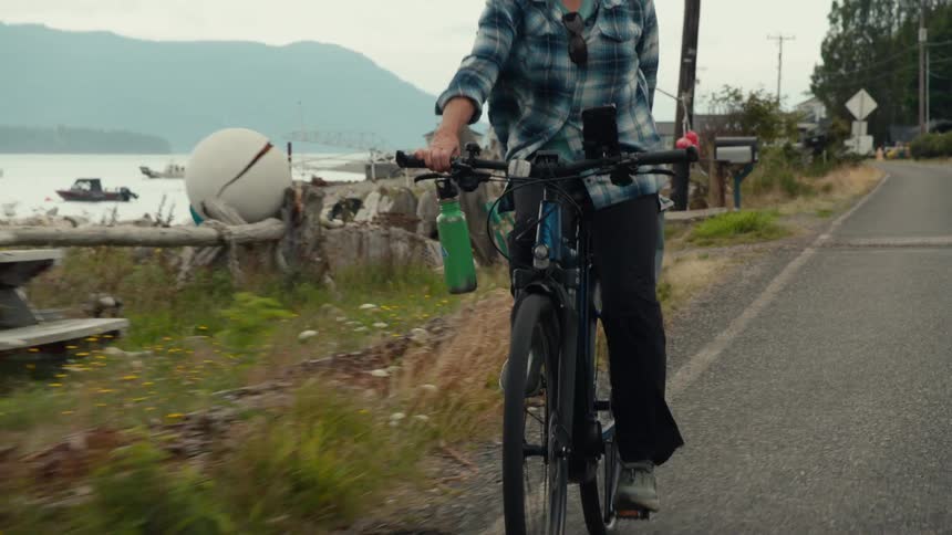A person rides a bicycle on a road near a waterfront