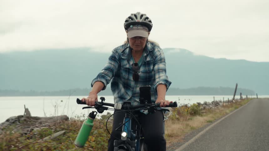 A woman wearing a helmet rides a bicycle along a road next to a body of water