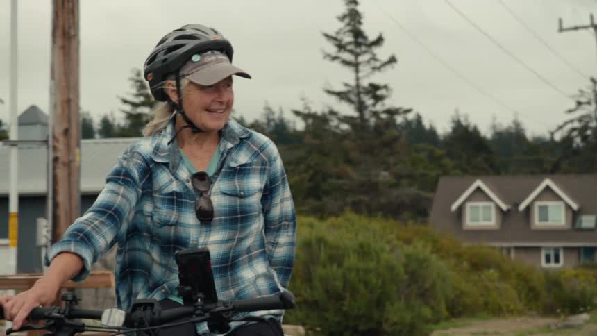 Older couple bicycles along a residential road near a conifer forest