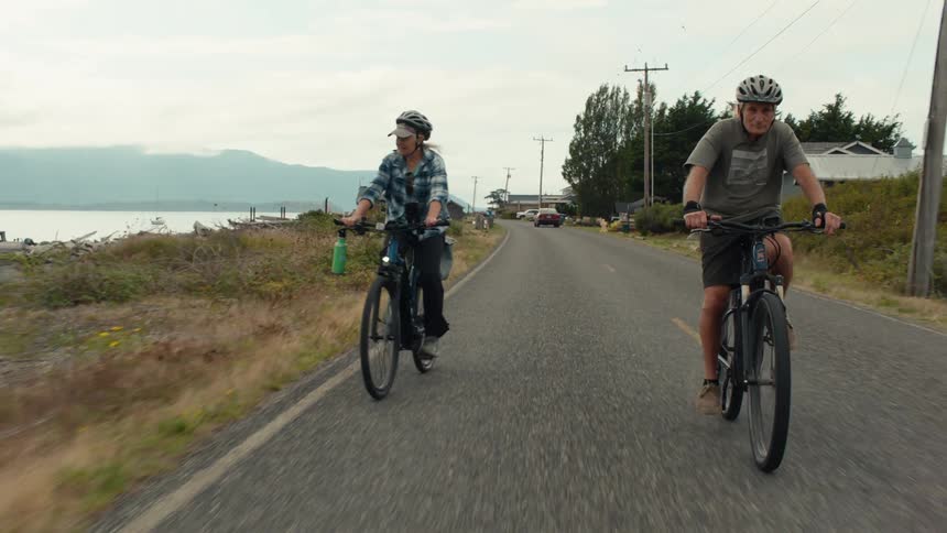 Two elderly people riding bicycles in a seaside setting