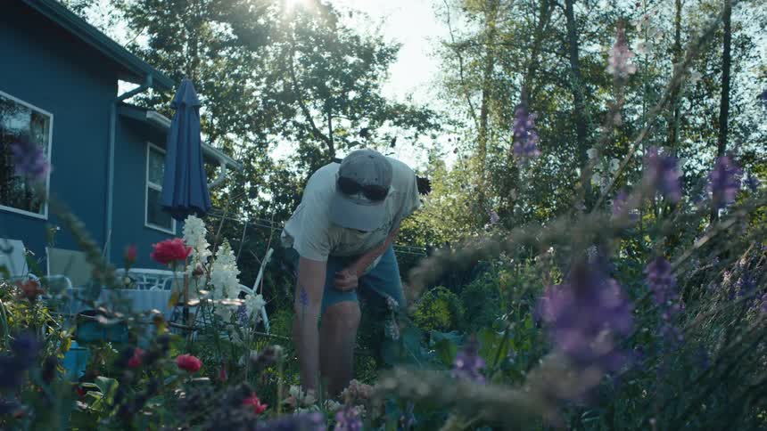 A woman tends to her vibrant flower garden surrounded by colorful blooms and lush greenery