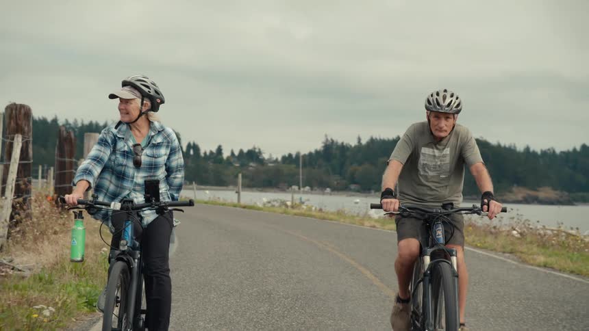A couple enjoying a bike ride together on a peaceful road near a scenic waterfront