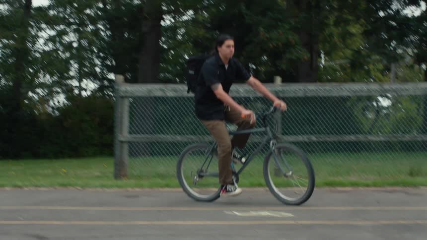 A man with a black backpack is riding a bicycle on a concrete floor and he is turning right