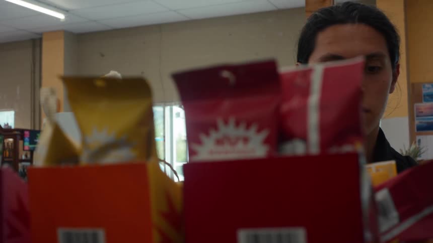 Close up of a person picking up snacks from a shelf in a convenience store