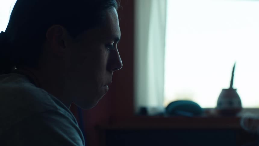 A sad looking man holds a burning cigarette while sitting in a room