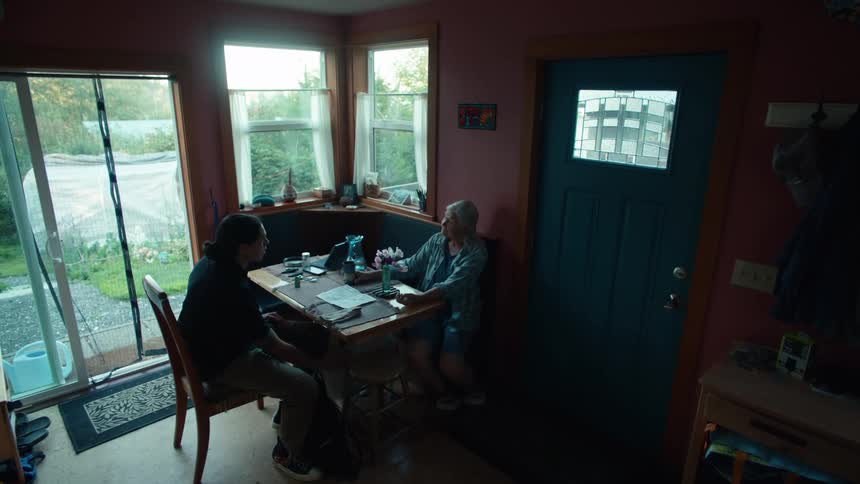 Man preparing bread dough and a lady and a young man sitting at the table next to him