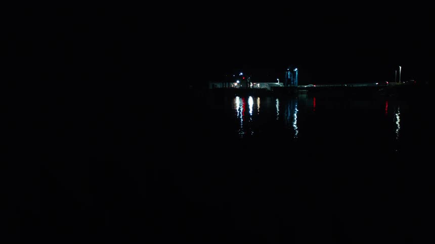 A ship illuminated by its lights sails across the dark water leaving a trail of reflections