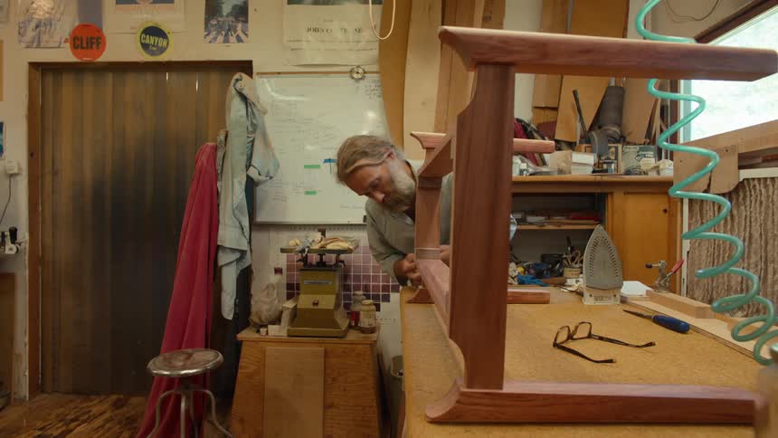 A well equipped woodworking workshop with a person working on a project with walls lined with tools and various woodworking equipment