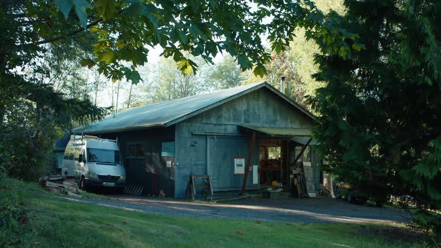 A serene workshop surrounded by greenery with a parked white van beside it