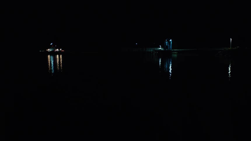 A boat sails on a lake with bright lights reflecting on the water at night
