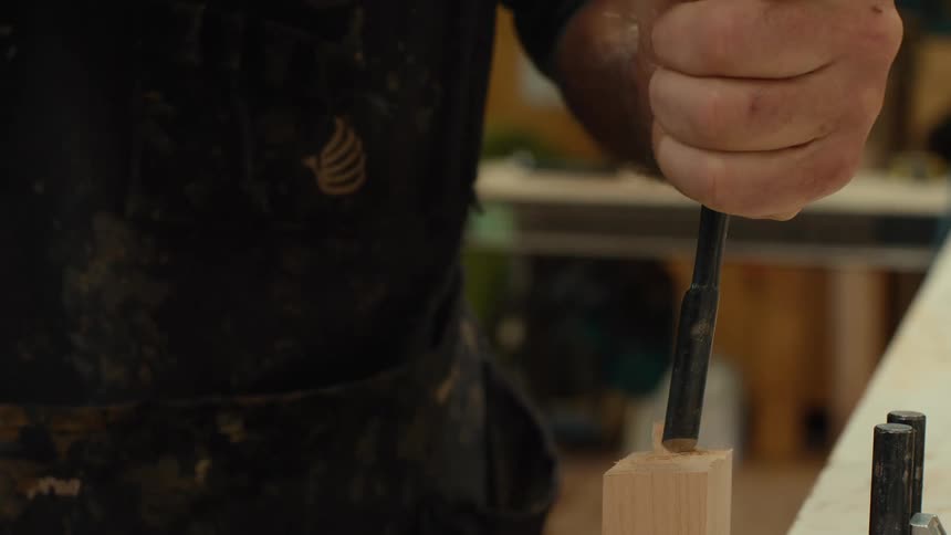 Hands of a carpenter working with a chisel on a piece of wood