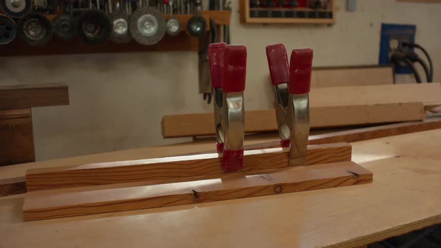 Two wooden planks are clamped together on a workbench with red clamps