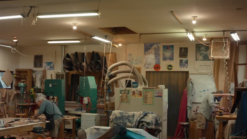 A well equipped woodworking workshop with two people working on projects with walls lined with tools and various woodworking equipment