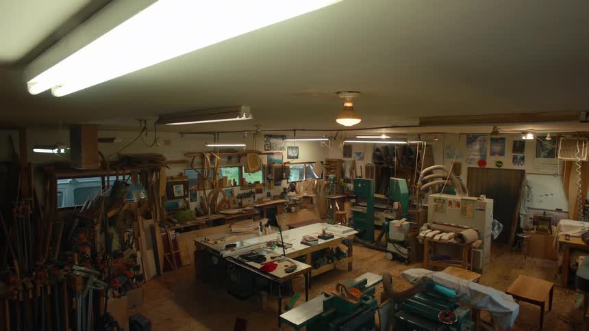 Lights illuminate a wellequipped woodworking workshop with various tools and materials scattered throughout