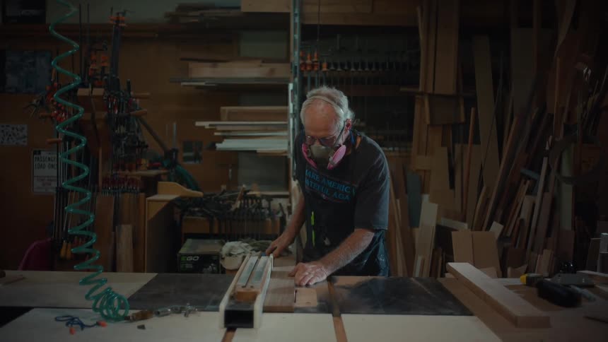 Male woodworker wipes sawdust from his arms after using a table saw in his workshop