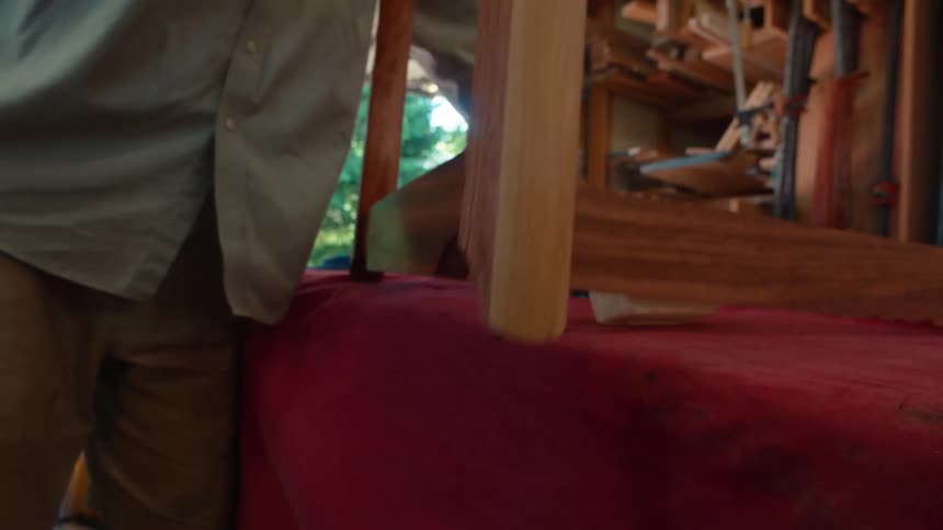A person is working on a wooden piece placed on a red cloth in a garage setting
