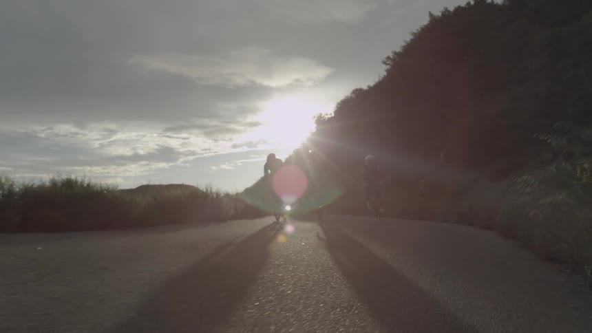 Three bicyclists are riding on a mountain road under a cloudy sky