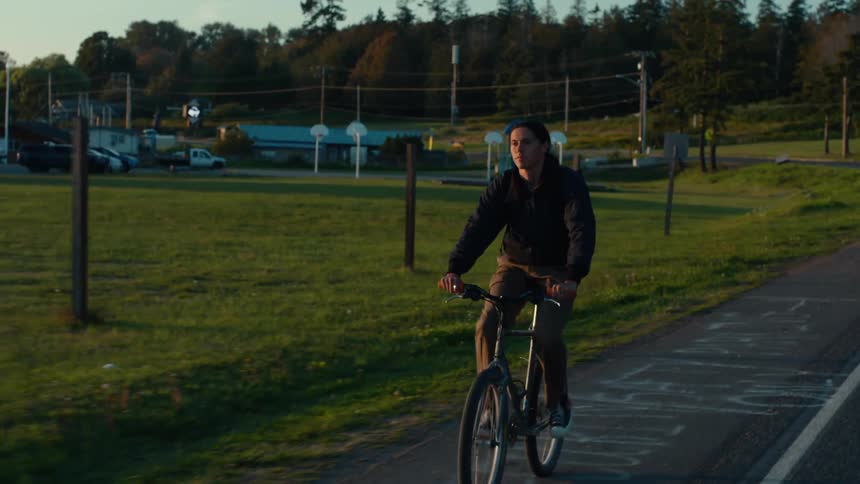 A young man rides a bicycle down a paved road at sunset